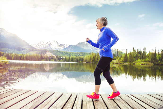 Senior woman in workout gear running alongside lake on a path
